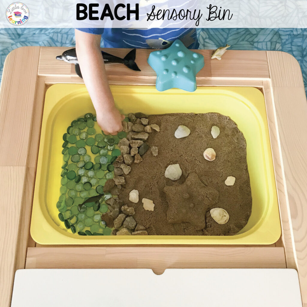 Preschool beach sensory bin with kinetic sand, seashells, blue gems, and sea animals.